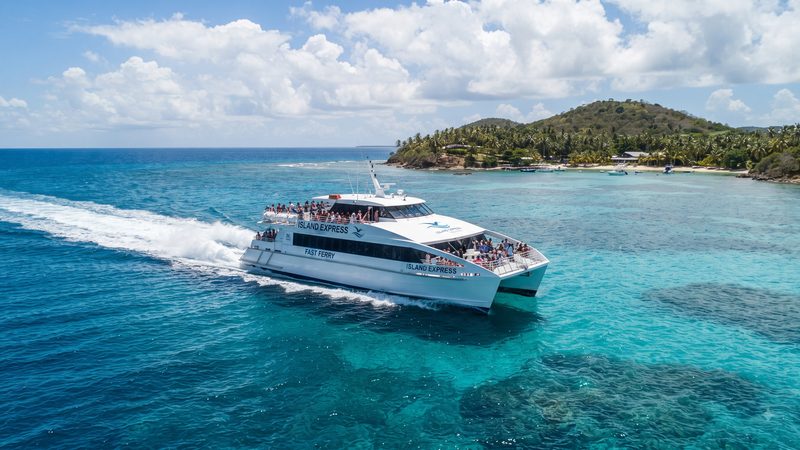 High-speed catamaran ferry crossing turquoise Bahamas water toward a tropical island