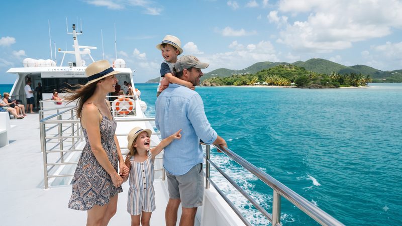 Family with two children at the deck railing of a ferry looking out over turquoise Caribbean water
