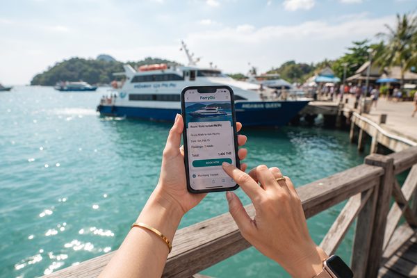 Hands booking ferry tickets on a smartphone with a ferry harbor in the background