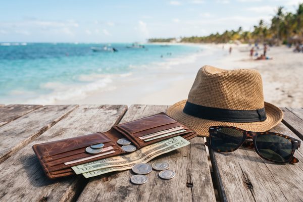 Open wallet with banknotes next to a straw hat at a tropical beach